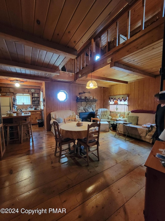 dining space with wood walls, beamed ceiling, a fireplace, hardwood / wood-style floors, and wooden ceiling