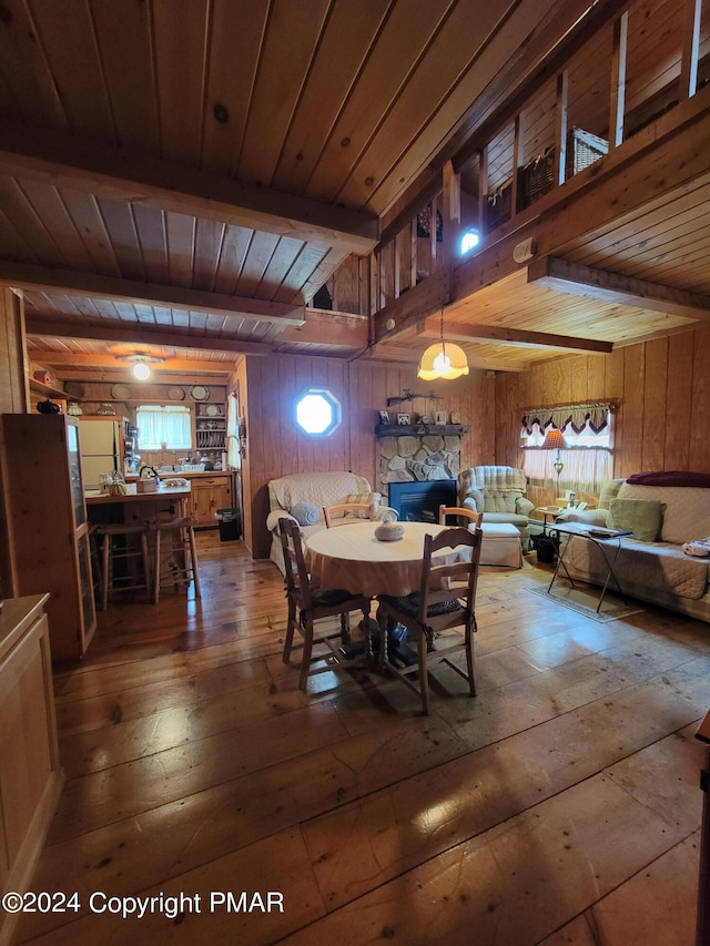 dining area with wood walls, beamed ceiling, a stone fireplace, hardwood / wood-style floors, and wood ceiling