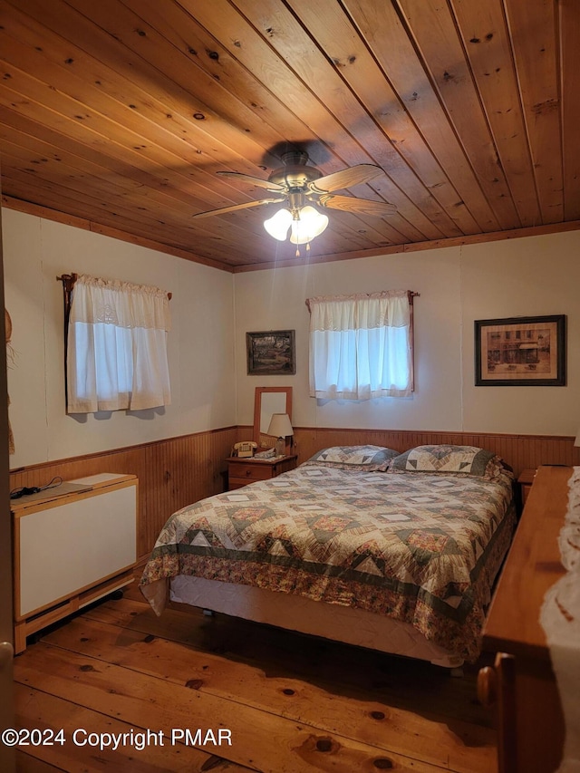 bedroom featuring wood walls, hardwood / wood-style floors, wood ceiling, a ceiling fan, and wainscoting