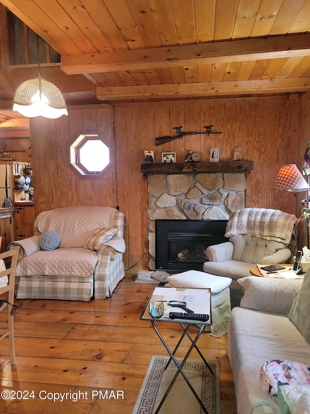 living area with wood walls, beamed ceiling, a stone fireplace, wood ceiling, and wood-type flooring