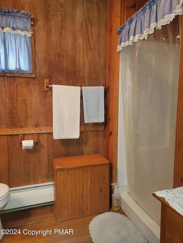 full bathroom featuring wood walls, a shower stall, a baseboard radiator, toilet, and wood finished floors