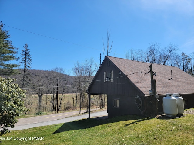 view of side of home with a lawn, an attached carport, a shingled roof, and concrete driveway