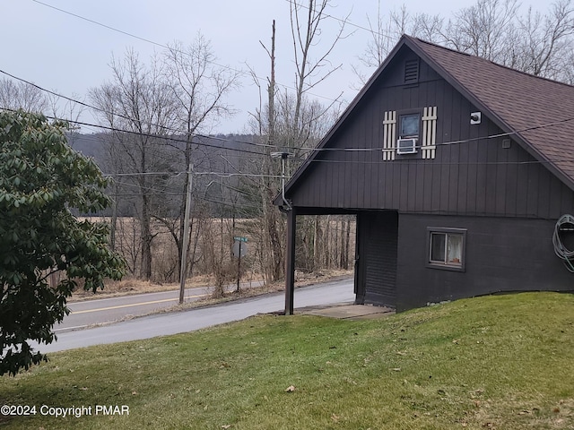 view of side of home with driveway, roof with shingles, and a lawn