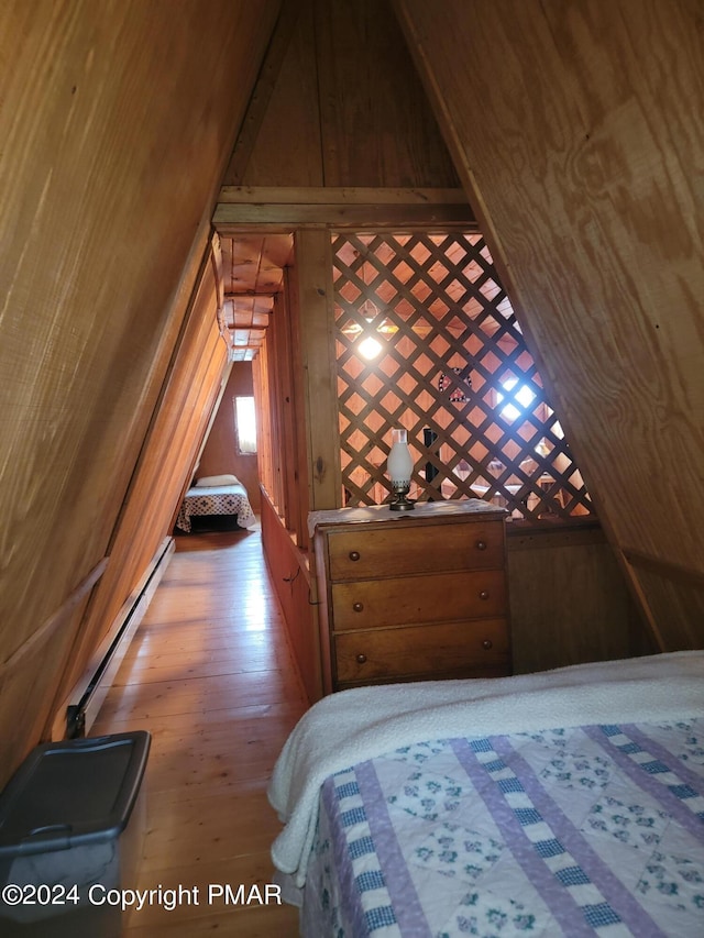 bedroom with a baseboard radiator, wood finished floors, and wood walls