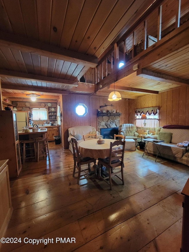 dining area featuring wood walls, a fireplace, beam ceiling, wood ceiling, and wood-type flooring