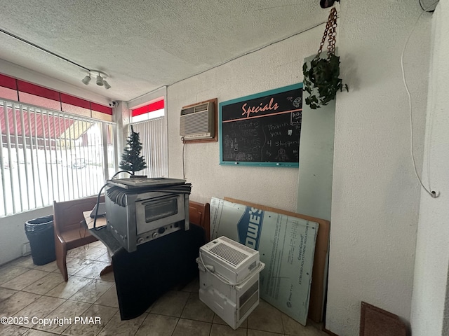 interior space with a wall mounted AC, a wood stove, a textured ceiling, tile patterned floors, and a textured wall