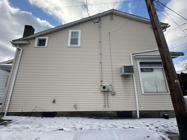 snow covered property with a wall mounted air conditioner and a chimney