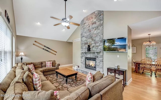 living room featuring visible vents, a stone fireplace, high vaulted ceiling, light wood-type flooring, and ceiling fan with notable chandelier