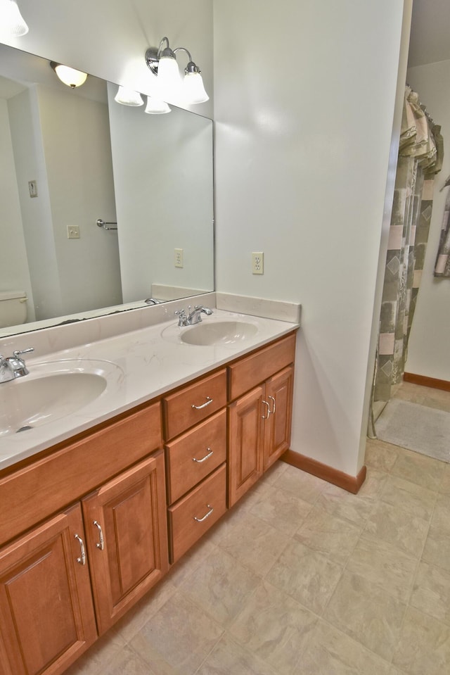 full bath with baseboards, toilet, double vanity, and a sink