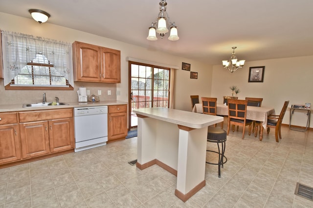 kitchen featuring a chandelier, brown cabinetry, light countertops, white dishwasher, and a sink