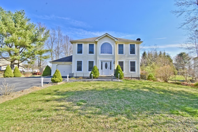 colonial-style house featuring fence, aphalt driveway, a front lawn, and an attached garage