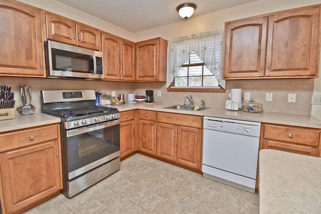kitchen with a sink, light tile patterned floors, brown cabinetry, light countertops, and appliances with stainless steel finishes