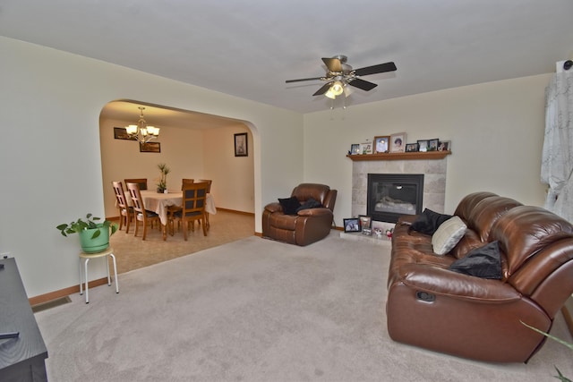 carpeted living area with a fireplace, arched walkways, baseboards, and ceiling fan with notable chandelier