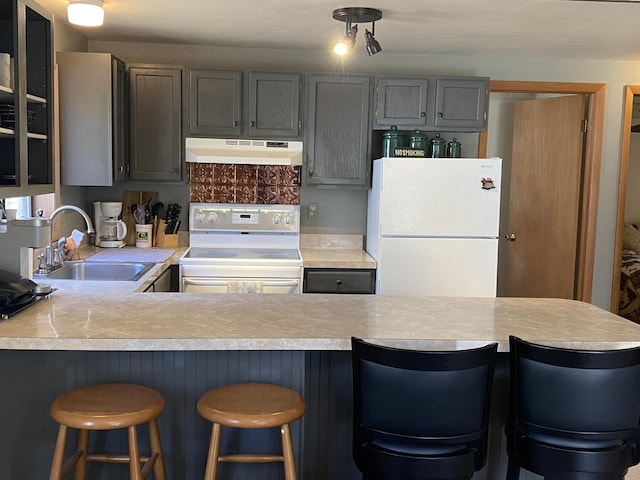 kitchen with a sink, under cabinet range hood, white appliances, a peninsula, and light countertops