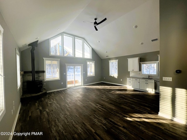 unfurnished living room featuring visible vents, dark wood-type flooring, a ceiling fan, a wood stove, and high vaulted ceiling