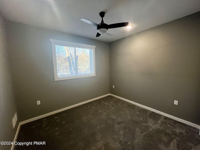 unfurnished room featuring visible vents, baseboards, dark carpet, and a ceiling fan