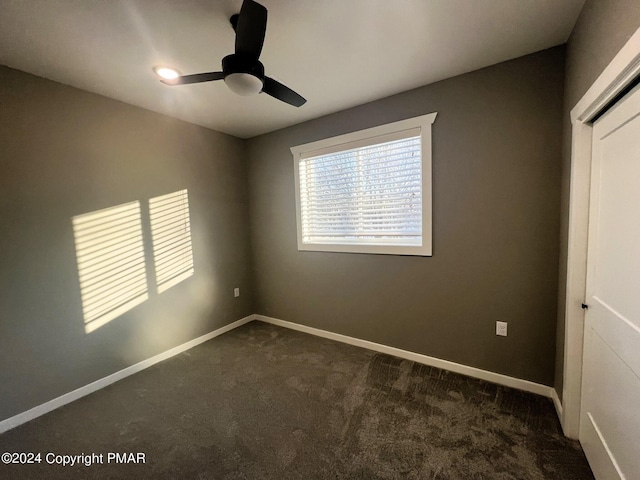 unfurnished bedroom with a closet, baseboards, dark carpet, and a ceiling fan