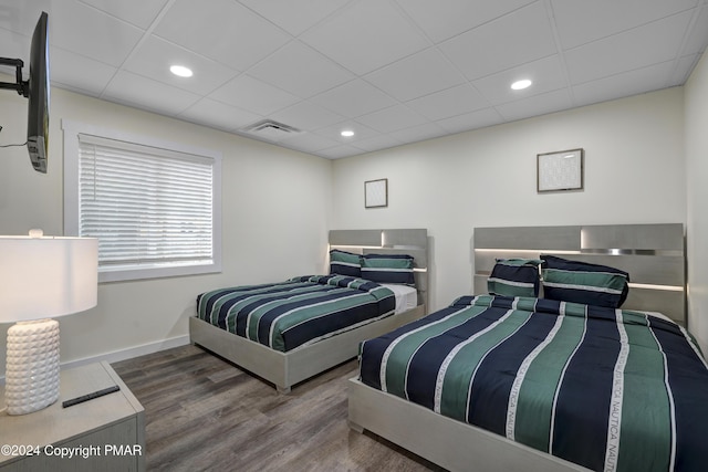 bedroom featuring a paneled ceiling, visible vents, baseboards, and wood finished floors