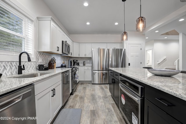 kitchen featuring stainless steel appliances, a sink, white cabinetry, tasteful backsplash, and decorative light fixtures