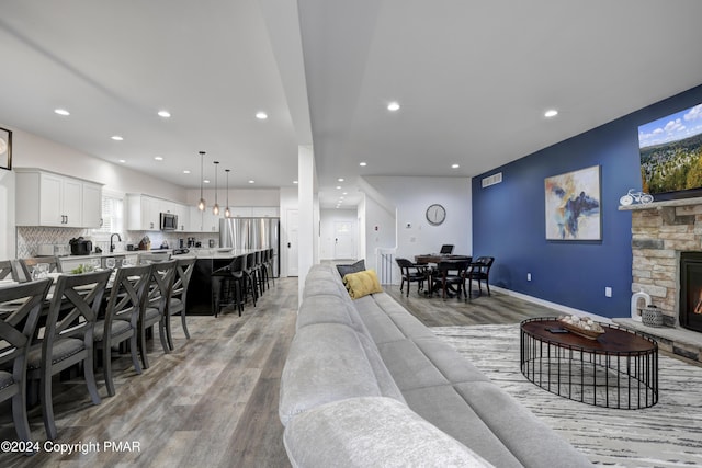 living area with light wood finished floors, recessed lighting, baseboards, and a stone fireplace