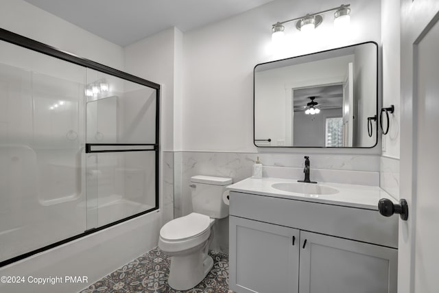 bathroom featuring enclosed tub / shower combo, toilet, vanity, tile walls, and wainscoting