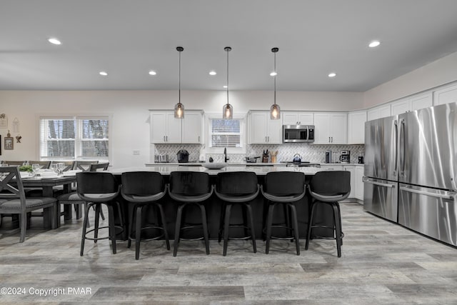 kitchen featuring white cabinetry, light wood-style floors, appliances with stainless steel finishes, backsplash, and a center island