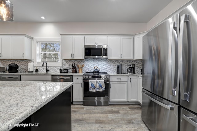 kitchen featuring light stone counters, decorative backsplash, appliances with stainless steel finishes, light wood-style floors, and white cabinets