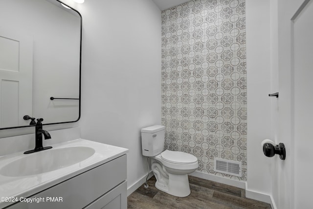 bathroom with visible vents, toilet, vanity, wood finished floors, and baseboards