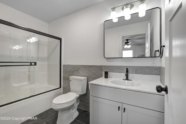 full bath featuring tile patterned flooring, toilet, vanity, tile walls, and wainscoting