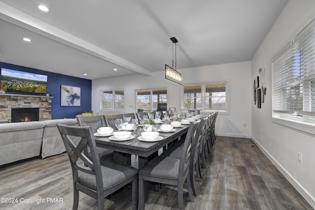 dining room featuring a healthy amount of sunlight, a fireplace, beamed ceiling, and wood finished floors