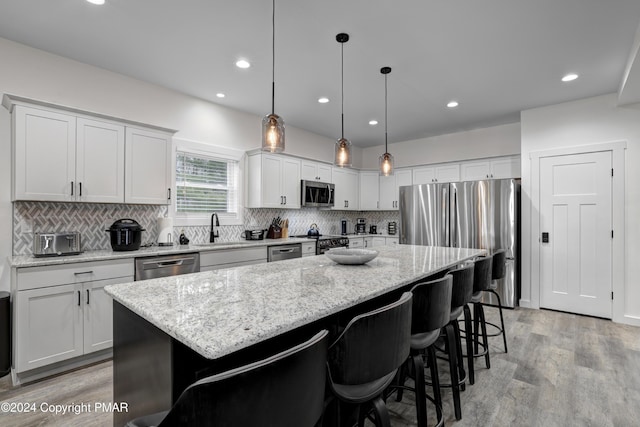 kitchen with a kitchen island, appliances with stainless steel finishes, light wood-type flooring, a kitchen bar, and backsplash