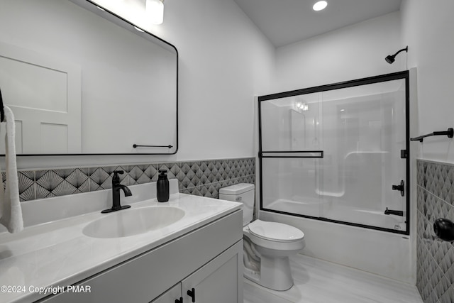 bathroom with shower / bath combination with glass door, wainscoting, vanity, and tile walls