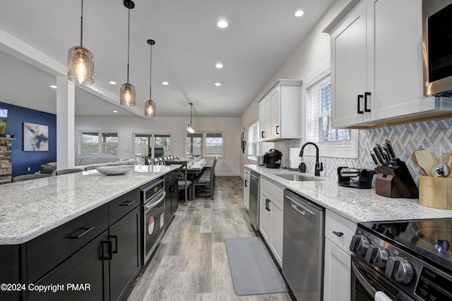 kitchen with tasteful backsplash, light stone countertops, stainless steel appliances, white cabinetry, and a sink