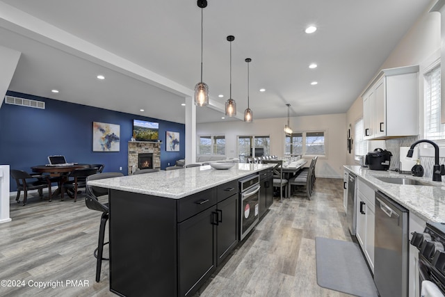 kitchen featuring a stone fireplace, dark cabinets, a sink, white cabinets, and appliances with stainless steel finishes