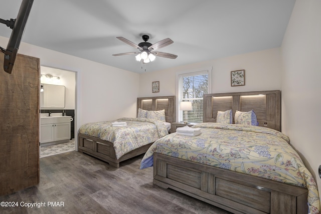 bedroom featuring ensuite bathroom, a barn door, a sink, wood finished floors, and a ceiling fan