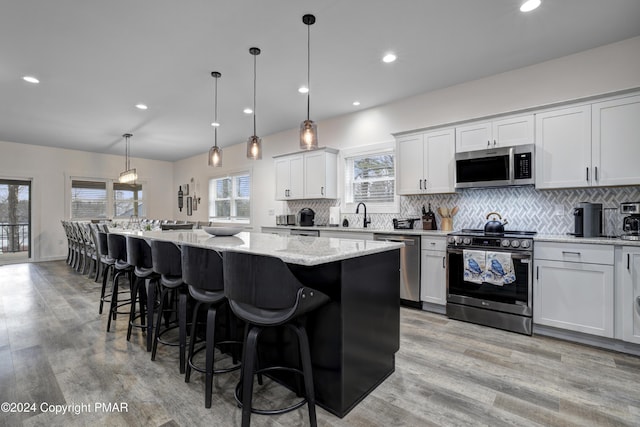 kitchen with a center island, stainless steel appliances, decorative backsplash, light wood-type flooring, and a kitchen breakfast bar