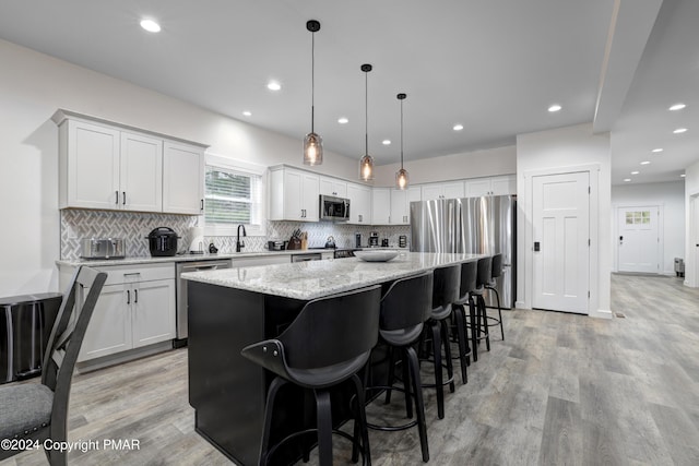 kitchen with decorative backsplash, a kitchen island, light stone counters, stainless steel appliances, and light wood-type flooring