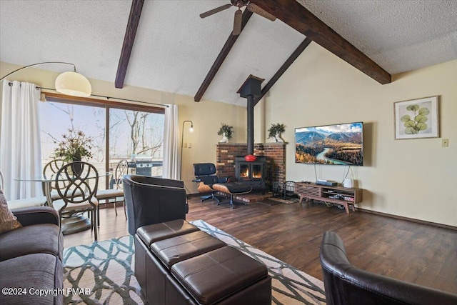 living area with a ceiling fan, wood finished floors, vaulted ceiling with beams, a wood stove, and a textured ceiling