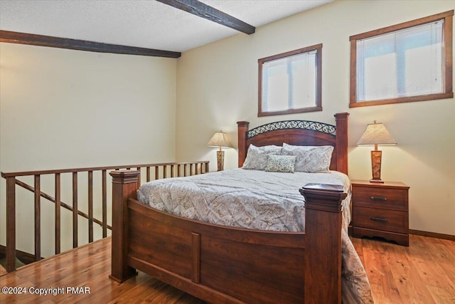 bedroom with beam ceiling, a textured ceiling, baseboards, and wood finished floors