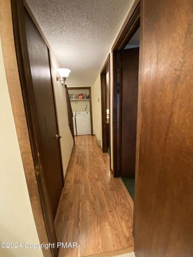 hallway with a textured ceiling, washing machine and clothes dryer, and wood finished floors