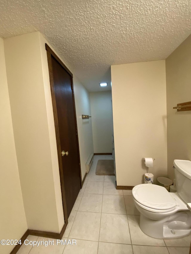 bathroom featuring a textured ceiling, tile patterned flooring, toilet, and baseboards