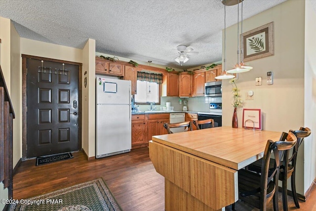 kitchen with light countertops, dark wood-type flooring, a sink, white appliances, and a peninsula