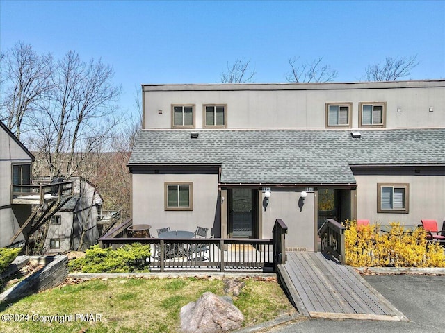 view of property with stucco siding, a deck, and roof with shingles