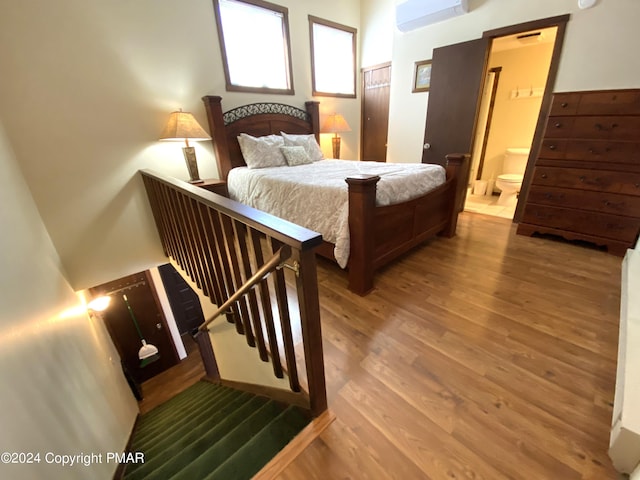 bedroom with ensuite bathroom, wood finished floors, and a wall mounted air conditioner