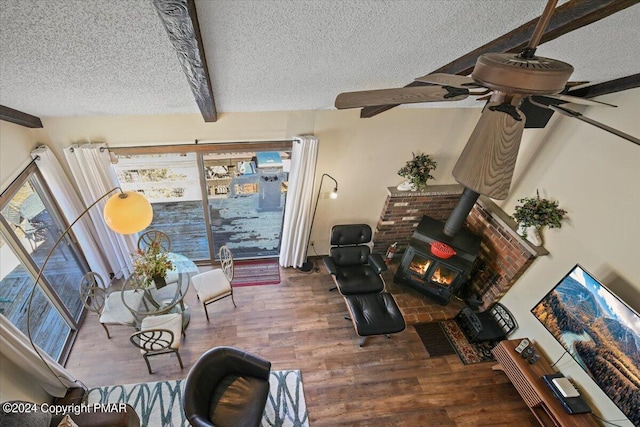 living area featuring a wood stove, beamed ceiling, a textured ceiling, and wood finished floors