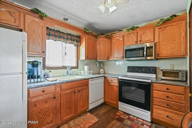 kitchen featuring dark wood-type flooring, white appliances, a sink, and backsplash