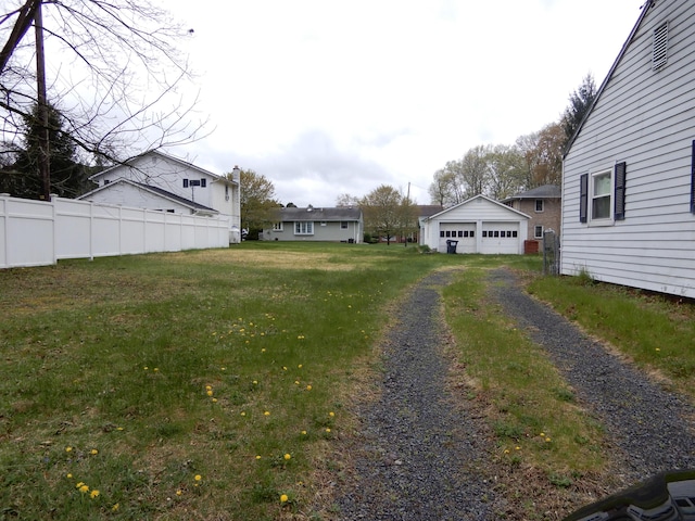 view of yard featuring a detached garage, fence, and an outbuilding