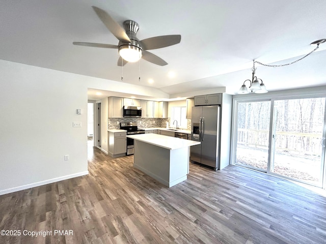 kitchen featuring stainless steel appliances, a kitchen island, a sink, gray cabinets, and backsplash