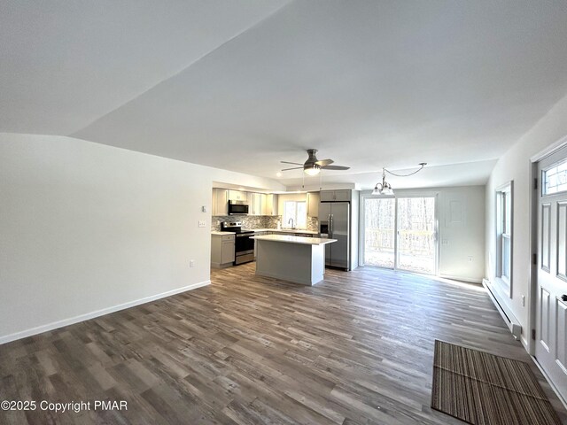 unfurnished living room featuring ceiling fan with notable chandelier, dark wood-type flooring, a healthy amount of sunlight, and baseboard heating