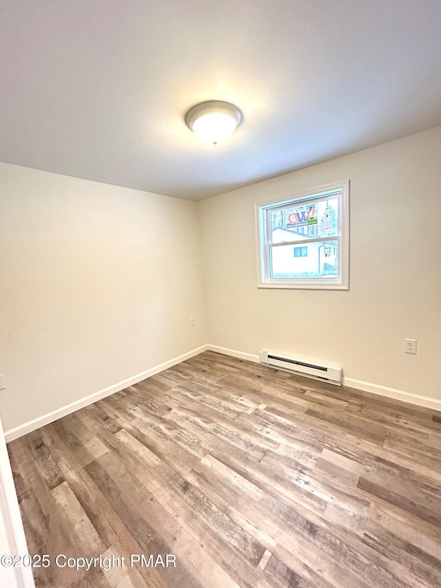 empty room with a baseboard heating unit, baseboards, and wood finished floors